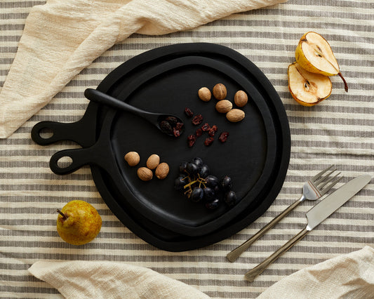 Black wood round serving board set with serving spoon on linen with assorted nuts and nibbles