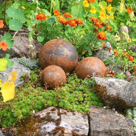 Rusted garden ball trio in flower borders weathered steel spheres cottage garden sculptures UK