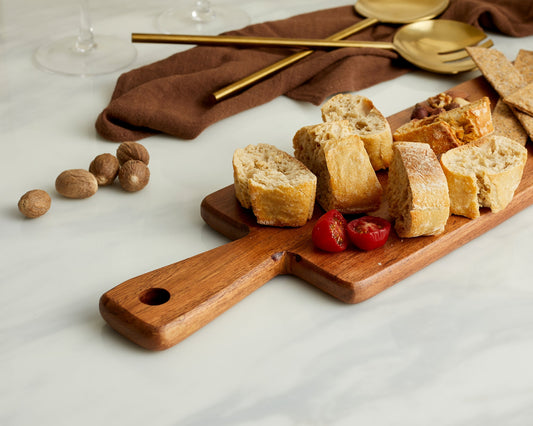 Close-up of acacia wood serving board on a marble worktop with servers, receipt book, and brown organza napkin