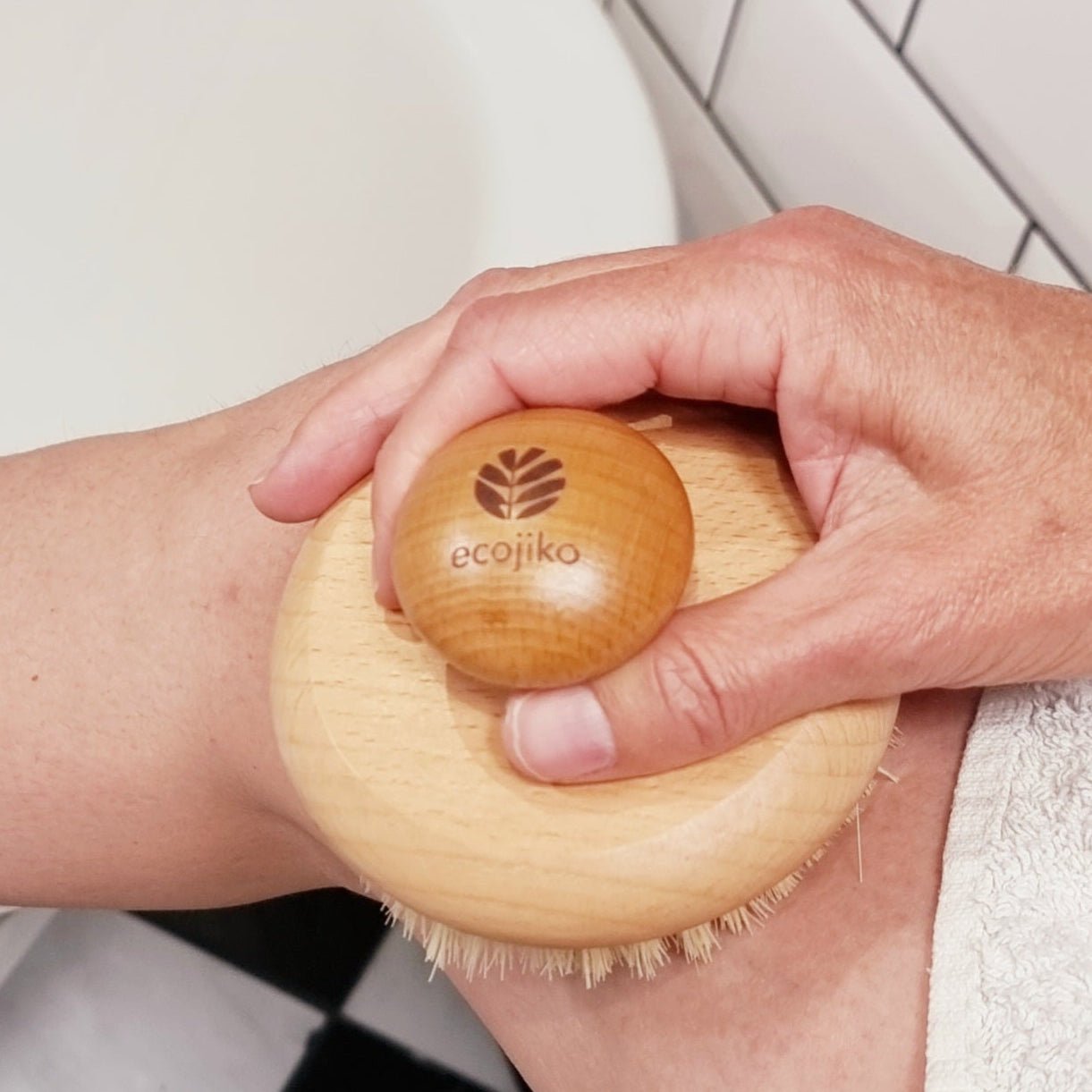 Natural wooden body brush in use during bathing ritual, shown in soft-lit bathroom with countryside-inspired styling