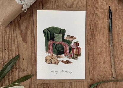 Christmas card with green armchair, dog resting, and wrapped gifts — cosy festive countryside warmth.