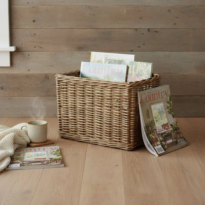 Antique wicker magazine rack with Country magazines on a wooden floor near a cozy knit blanket and steaming cup