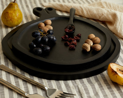 Alternate close view of black wood round serving board set with serving spoon on linen with nuts and nibbles