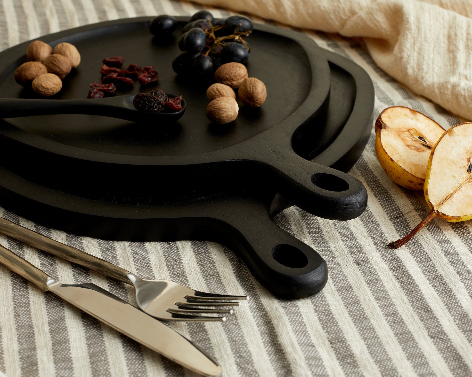 Close view of black wood round serving board set with serving spoon on linen with nuts and nibbles