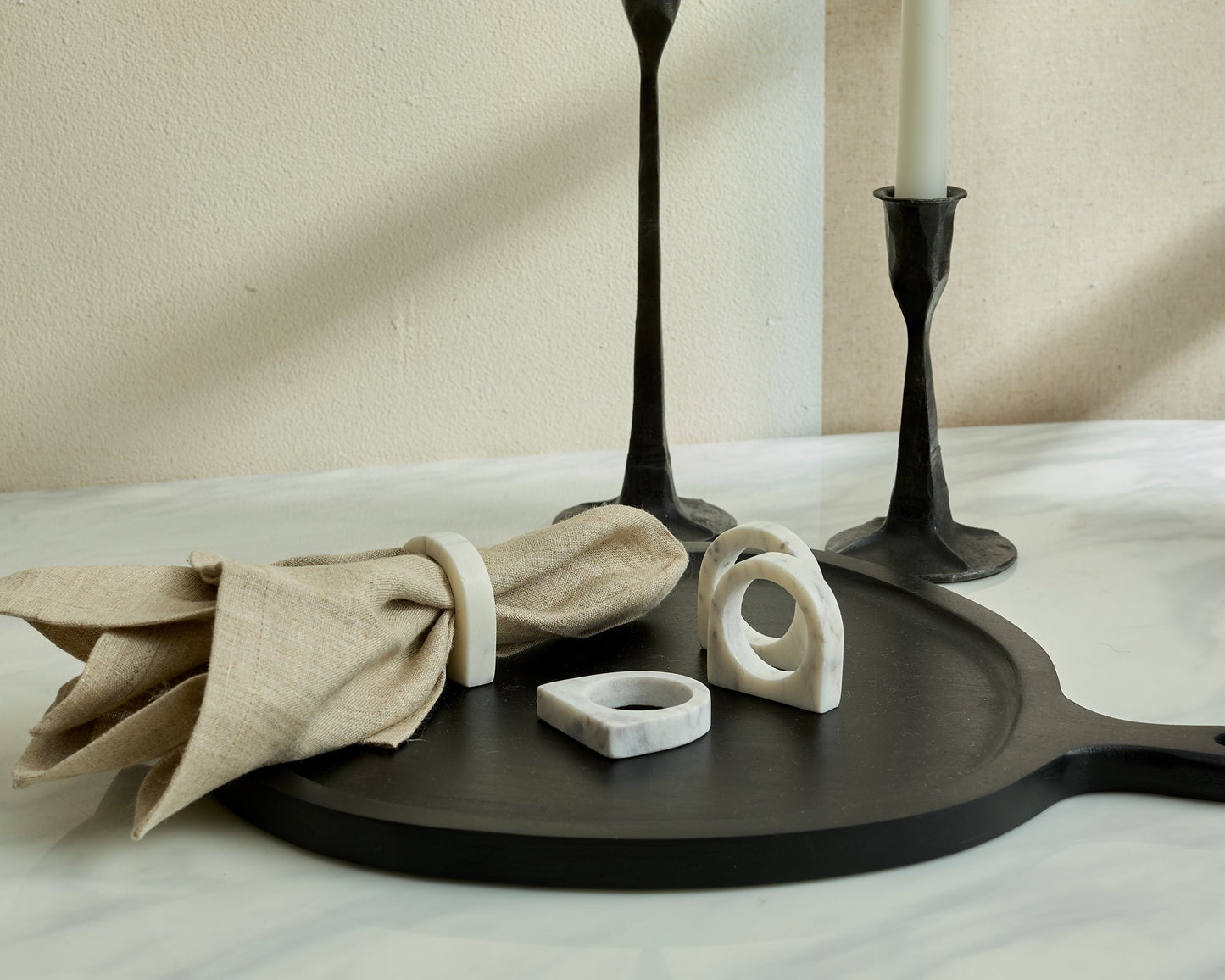 Beige linen napkin on a black serving board with marble napkin rings and candle holders.