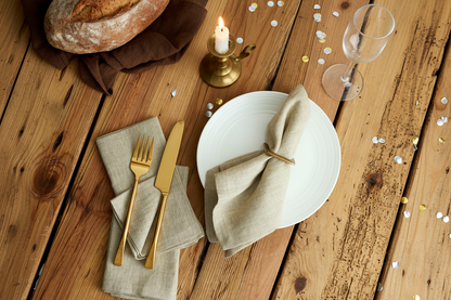 Beige linen napkin on a celebration table with gold cutlery and confetti.