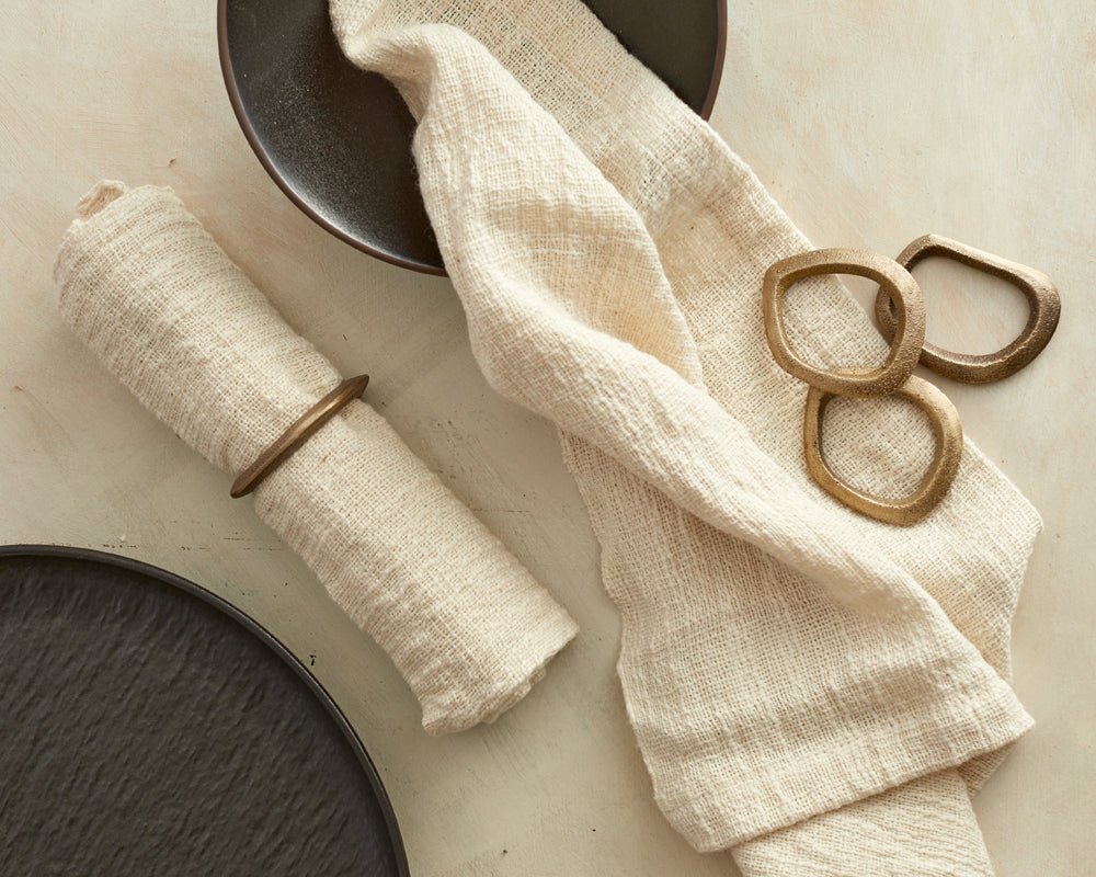 The Elmsley brass napkin rings set of 4 styled on table with linen napkins and black plates
