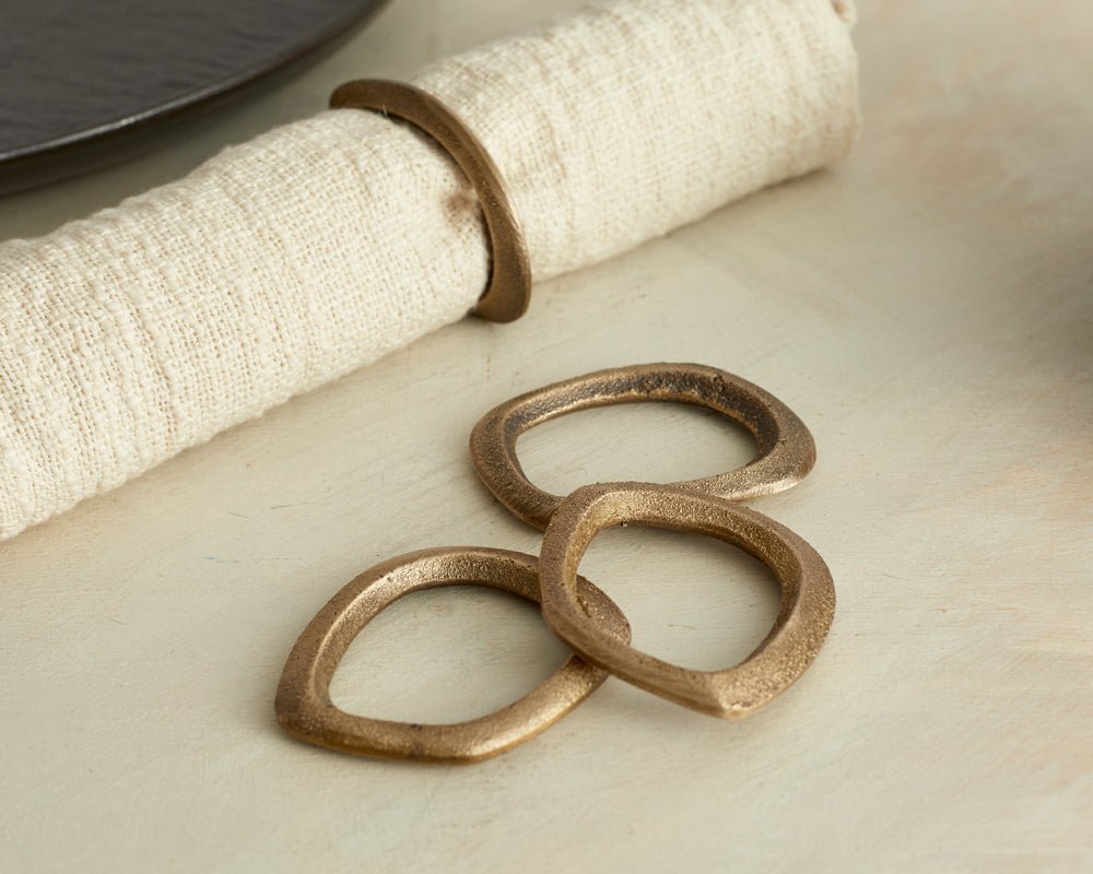 The Elmsley brass napkin rings set of 4 styled on table with linen napkin and black plate from another angle
