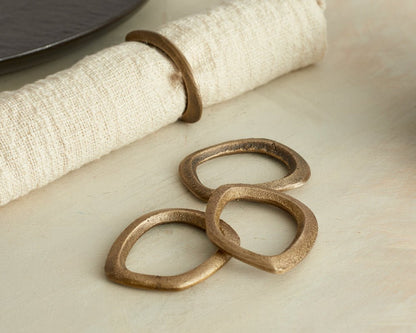 The Elmsley brass napkin rings set of 4 styled on table with linen napkin and black plate from another angle
