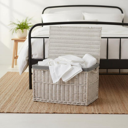 Large whitewash wicker basket with bed linens in cottage bedroom - Edith UK