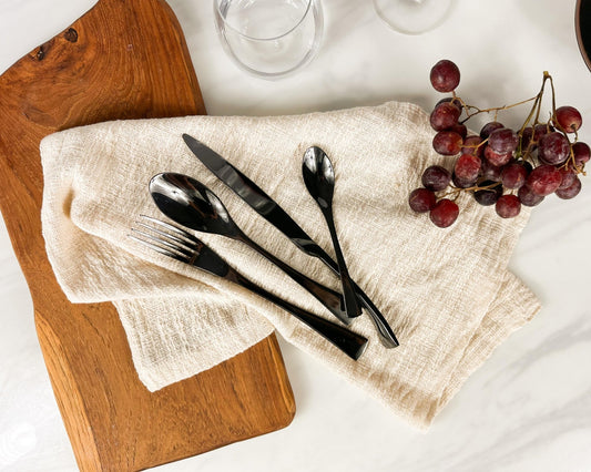 Matte black cutlery set stainless steel Ravenswell styled on natural linen napkin surrounded with grapes and serving board
