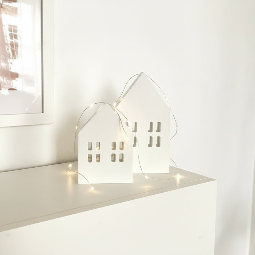 Scandi wooden Christmas village houses Nordic decoration styled on mantle with glowing fairy lights
