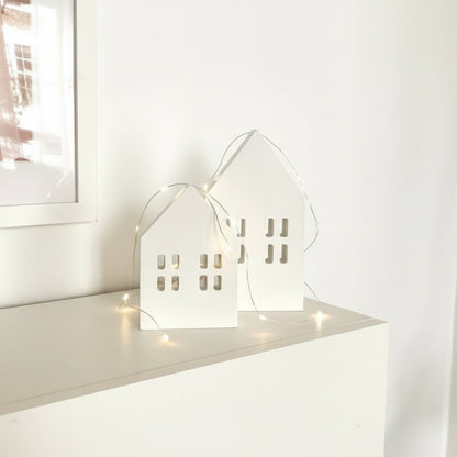 Scandi wooden Christmas village houses Nordic decoration styled on mantle with glowing fairy lights
