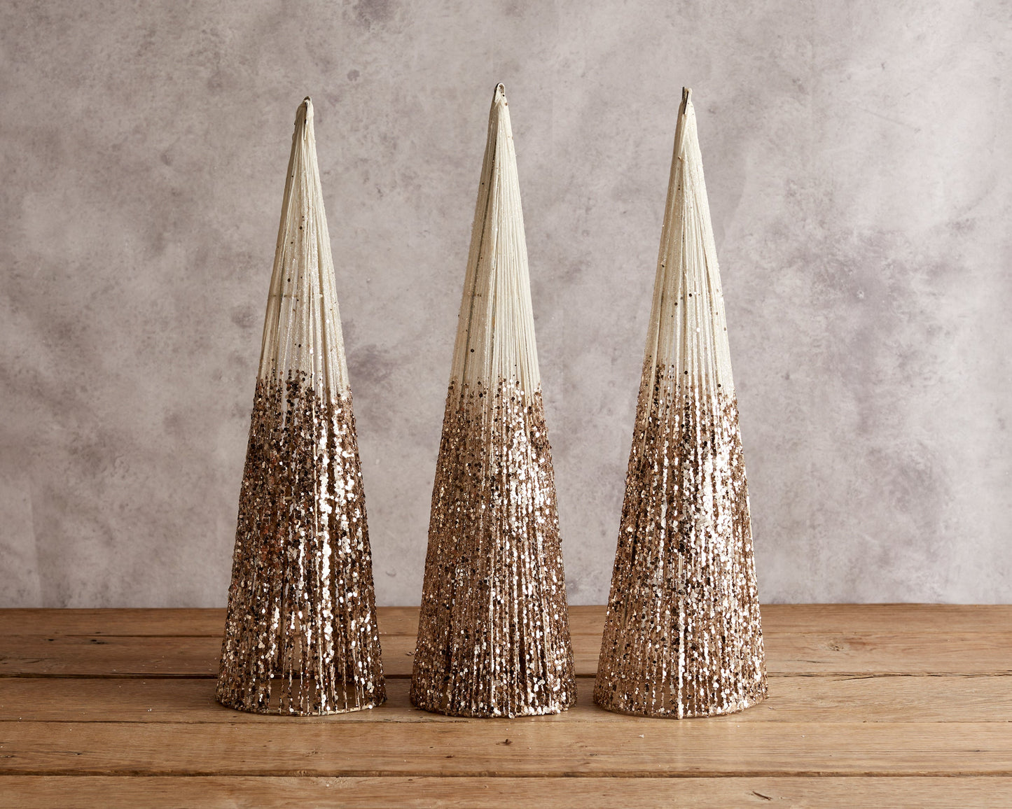 Set of three snowed Christmas cone trees festive mantel decorations on wooden table with candle and sprig
