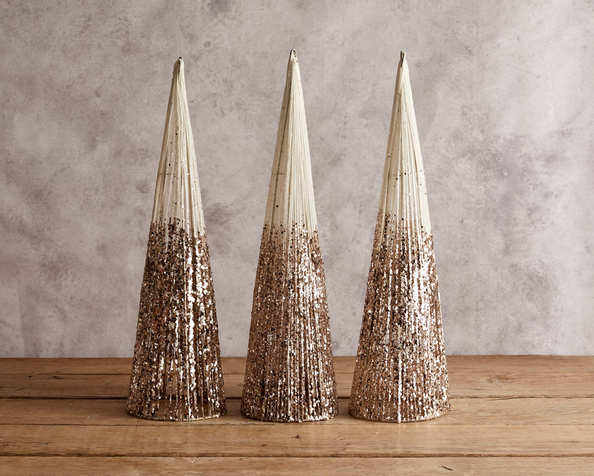 Set of three snowed Christmas cone trees festive mantel decorations on wooden table with candle and sprig
