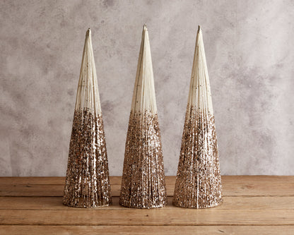 Set of three snowed Christmas cone trees festive mantel decorations on wooden table with candle and sprig
