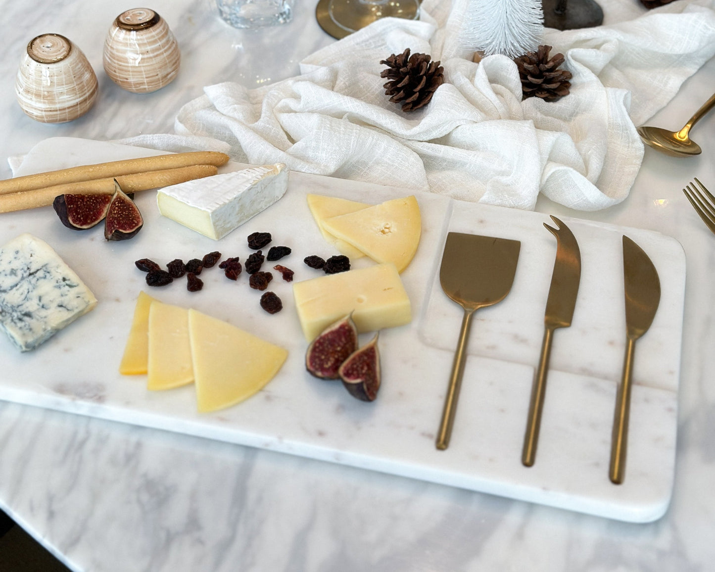Alternate view of white marble cheese board with stainless steel cutlery set, cheese, raisins, fig and breadsticks
