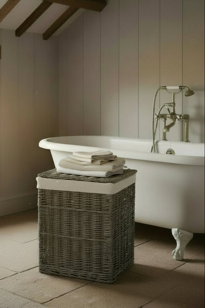 Large square wicker laundry basket antique wash beside roll top bath in period property bathroom
